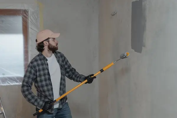 Painter rolling grey paint onto an interior wall in Manchester